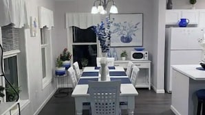Uma cozinha moderna com armários brancos, uma mesa de jantar com jogos americanos azuis e um lustre central.
