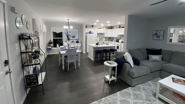 Uma sala de estar moderna com um sofá cinzento, uma mesa de centro e um espaço de jantar com uma mesa e cadeiras brancas.