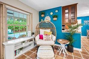 A cozy room with a large window, a wicker chair with cushions, a small table, and a potted plant. - Sunny Palms Villa - Heated Pool + Hot Tub, 2 miles to the Beach! (Fort Lauderdale)