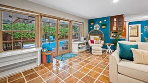 A spacious living area with large windows, a tiled floor, a white sofa, and a blue accent wall. - Sunny Palms Villa - Heated Pool + Hot Tub, 2 miles to the Beach! (Fort Lauderdale)