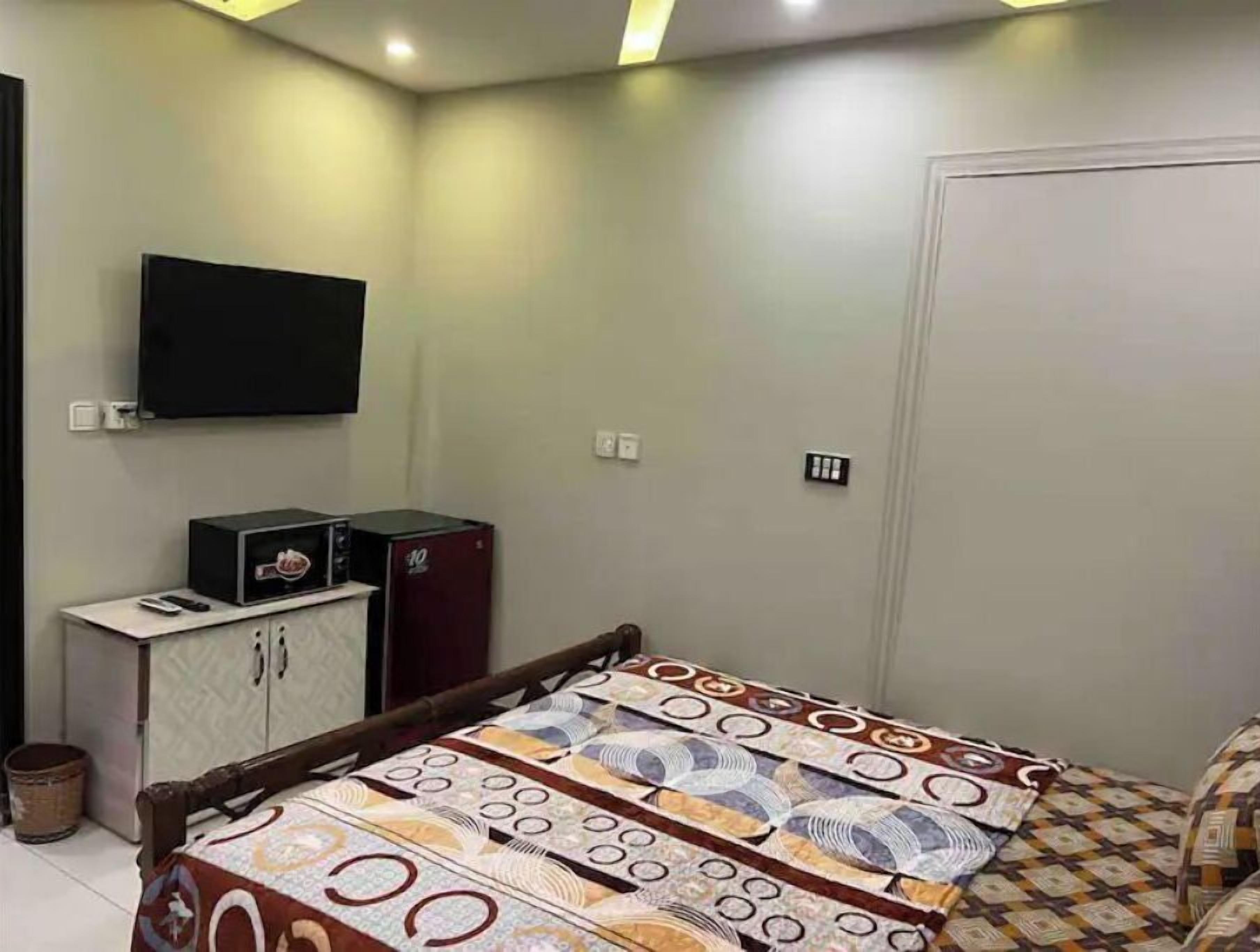 Un dormitorio con cama, televisión montada en la pared, armario y un mueble pequeño.