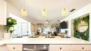 A modern kitchen with a large island, pendant lights, and a decorative wreath on the wall.