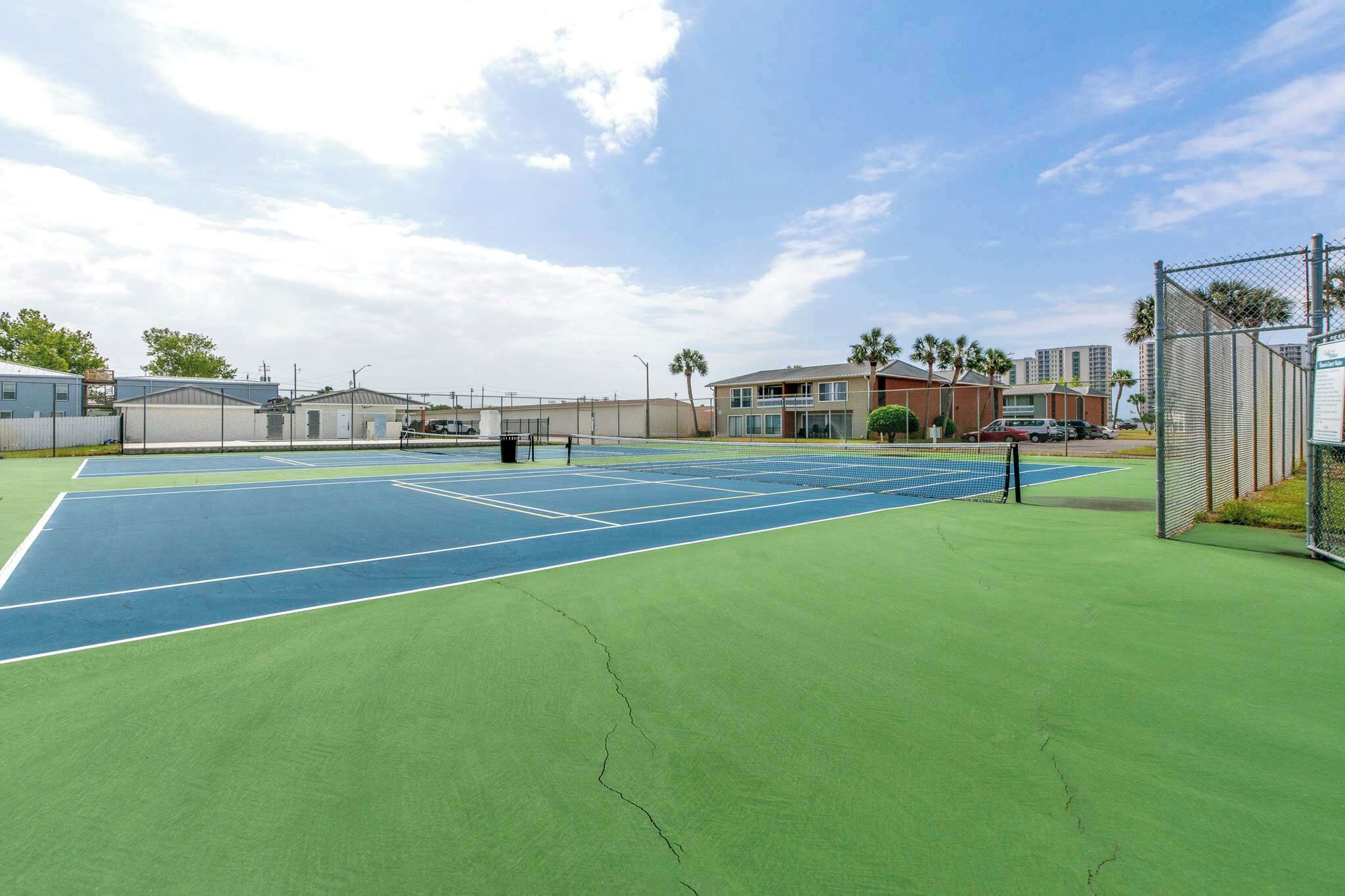 A tennis court with a net, surrounded by buildings and a fence.