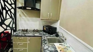 Een compacte keuken met een gasfornuis, een magnetron en een spoelbak. Er zijn kastjes en een decoratieve zwarte scheiding.'