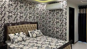 Een slaapkamer met een wand met geometrisch patroon, een gestuikt hoofdbord en een bed met een geborduurd sprei.