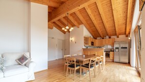 A spacious living area with a wooden dining table and chairs, a sofa, and a kitchen with wooden cabinets and a refrigerator.