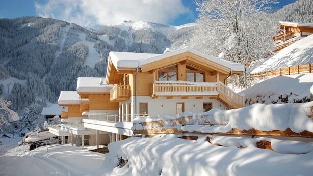 A wooden chalet with a balcony, surrounded by snow-covered mountains.