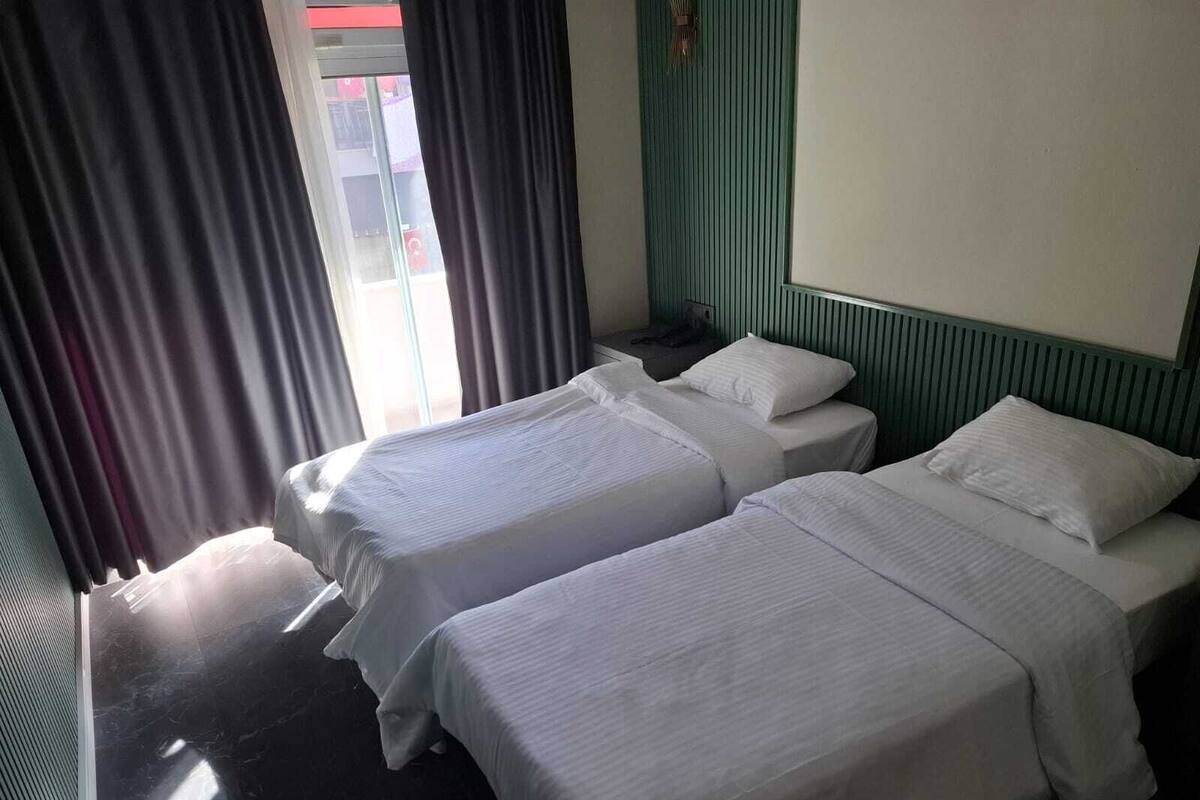 Une chambre d’hôtel avec deux lits simples, une fenêtre avec des rideaux et un mur vert.