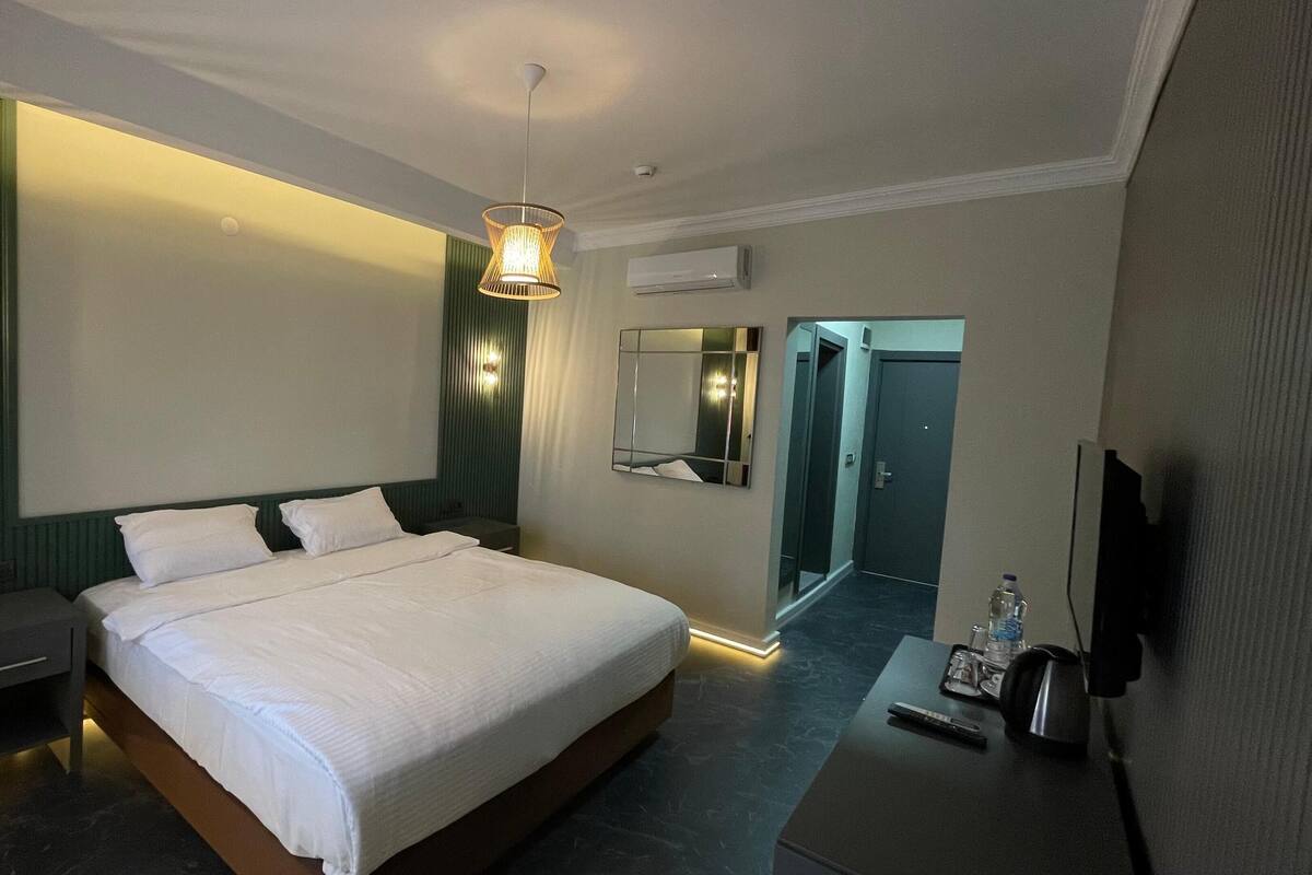Une chambre d’hôtel moderne dotée d’un grand lit, de tables de chevet, d’un bureau avec une chaise, d’une télévision et d’un miroir.
