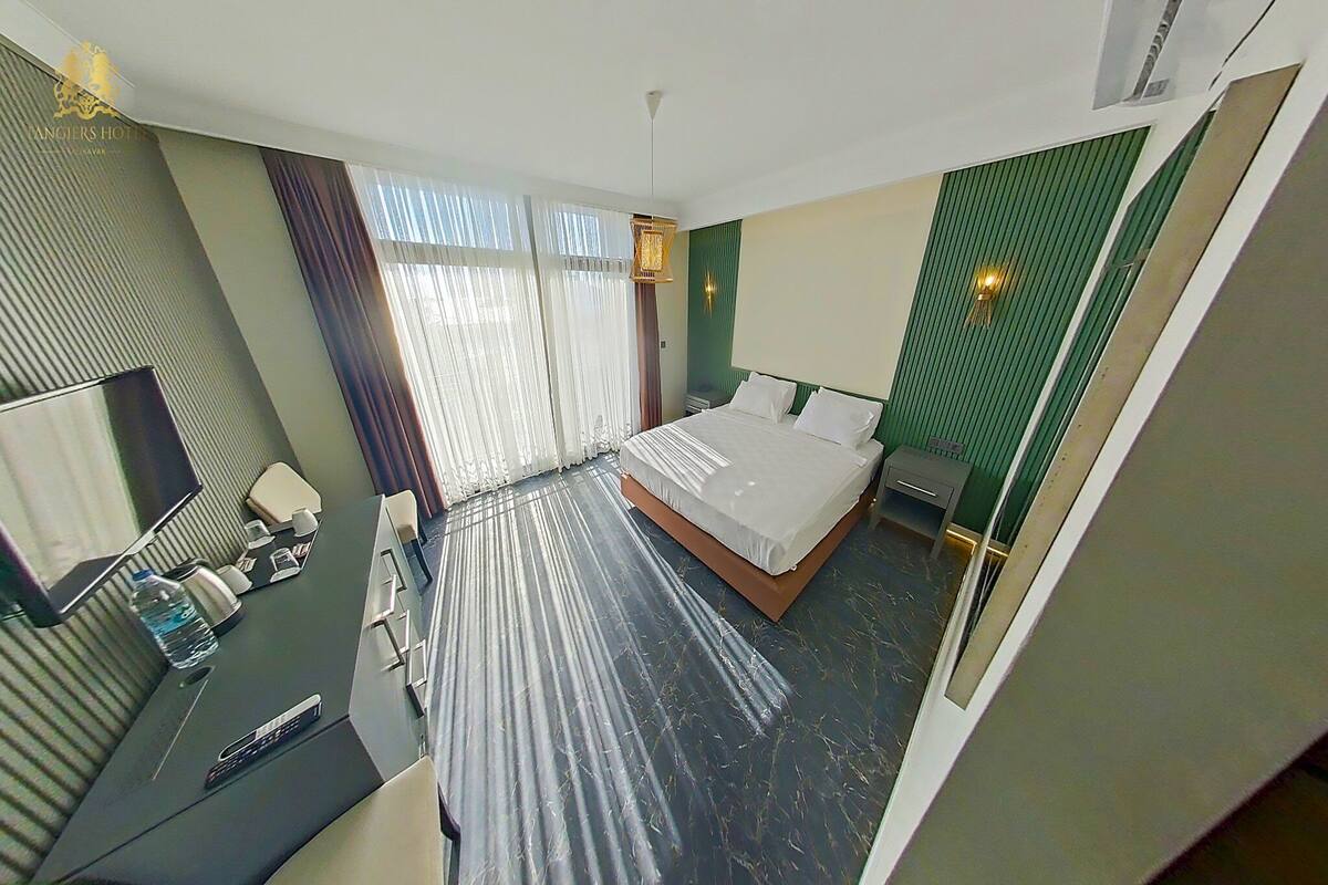 Une chambre d’hôtel comprenant un lit, un bureau avec une chaise, une télévision et une fenêtre avec des rideaux.