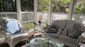 A wicker sofa with patterned cushions, a glass coffee table, and a small white side table with a lamp.