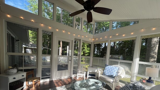 A sunroom with large windows, a ceiling fan, and a glass coffee table.