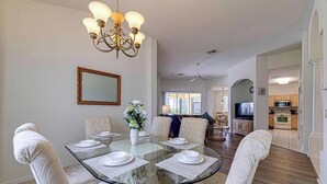 A dining area with a glass table, cushioned chairs, a chandelier, and a view into the living room. - Gorgeous 4 Bedroom, Disney And South Facing Pool (Davenport)