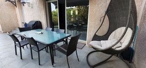 A patio with a glass table and chairs, a wicker chair, and a sliding glass door leading to an outdoor area. - 2 bedrooms with private bathroom and kitchen in shared villa with  swimming pool (Saint-Raphaël)