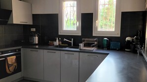 Una cocina moderna con gabinetes blancos, horno empotrado, campana extractora de acero inoxidable y una ventana con vista a la vegetación.
