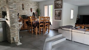 Una sala moderna con pared de ladrillo, un comedor con sillas y mesa de madera, un sofá gris y un televisor sobre un mueble de madera.