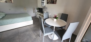 A compact room with a bed, a small dining table with chairs, a TV, and a wall-mounted shelf. - 2 bedrooms with private bathroom and kitchen in shared villa with  swimming pool (Saint-Raphaël)