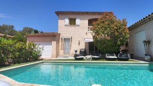 Una piscina con sillas de descanso, un patio y un edificio con techo de tejas y contraventanas.