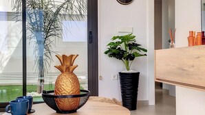 A modern living room with a round wooden table, a large window with a view of greenery, a wall-mounted clock, and a potted plant. - Villa with private roof terrace, patio with pool (Santiago de la Ribera)