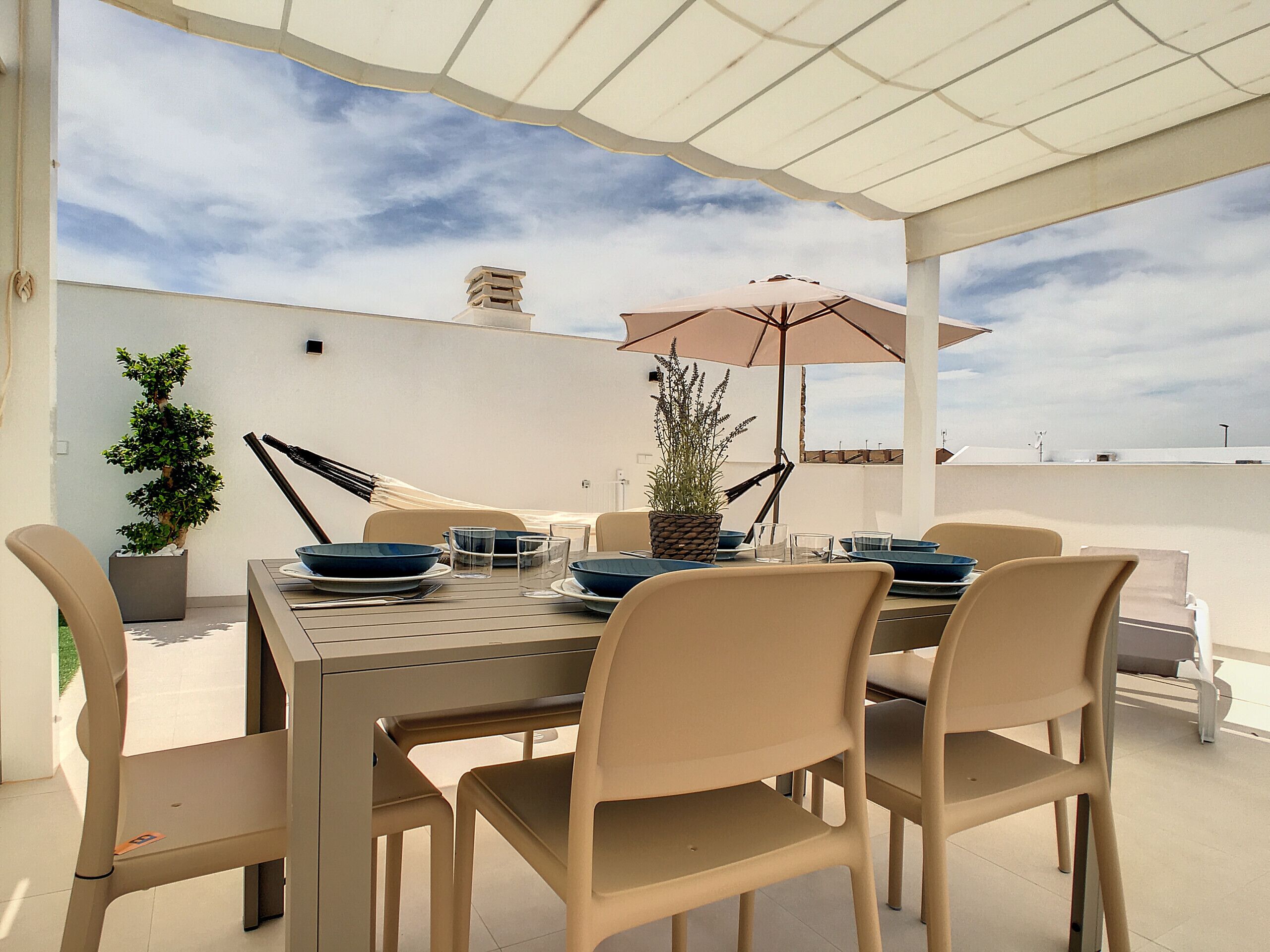 Une terrasse extérieure avec une table dressée pour le repas, entourée de chaises, et protégée par un auvent.