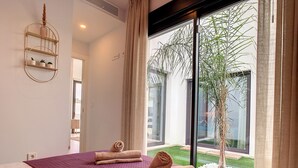 A modern bedroom with a large bed, a built-in shelf with decorative items, and a view of a garden through a sliding glass door. - Villa with private roof terrace, patio with pool (Santiago de la Ribera)
