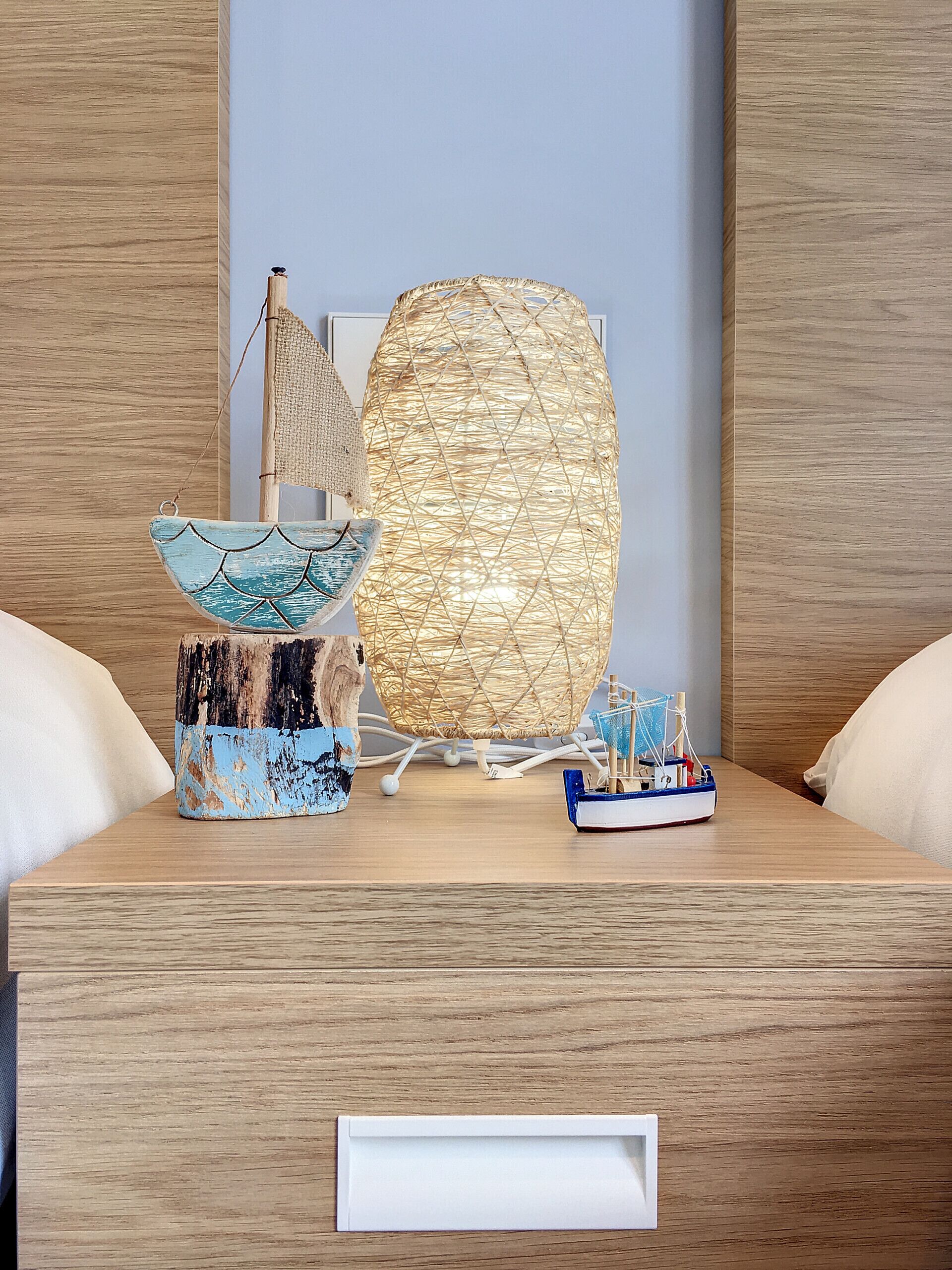 A wooden table with a decorative lamp, a small sailboat model, and a textured vase.