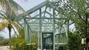 A glasshouse structure with a metal frame, surrounded by gravel and greenery. -  Starfish Cottage - Summer fun.  Sleeps 4 -boating fishing and Lobster 🦞 season. (Summerland Key)