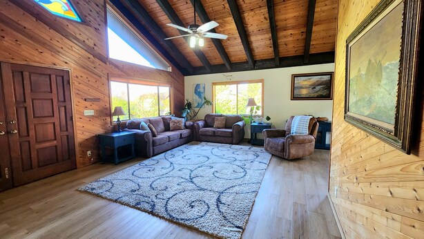 A spacious living room with wooden floors, a large sectional sofa, a ceiling fan, and a stained glass window. - Spacious home with large yard and hot tub- Nearby beach access and dog Friendly! (Brookings)