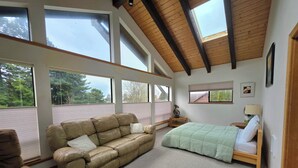 A bedroom with a large window, a sofa, a bed, and a nightstand. - Spacious home with large yard and hot tub- Nearby beach access and dog Friendly! (Brookings)