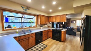 A kitchen with wooden cabinets, a black stove, and a window with a view of the outdoors. - Spacious home with large yard and hot tub- Nearby beach access and dog Friendly! (Brookings)