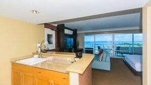 Une chambre d’hôtel moderne dotée d’une grande fenêtre, d’un balcon, d’un coin cuisine et d’un lit.