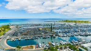Un port de plaisance où sont amarrés de nombreux bateaux, un espace de stationnement et une vue dégagée sur l’océan.