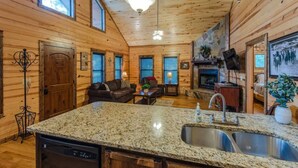 Un intérieur de chalet chaleureux avec des murs en bois, une cheminée en pierre, un îlot de cuisine en granit et un coin repas.