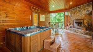 Une cabane en bois dotée d’un bain à remous, d’une cheminée en pierre et d’un balcon avec coin salon extérieur.