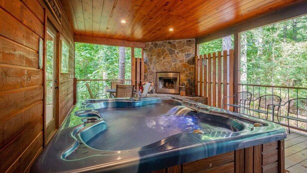 Un espace avec un bain à remous, une cheminée en pierre, une terrasse en bois et une vue sur la forêt.