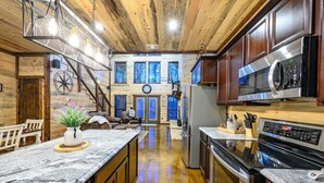 A spacious kitchen with wooden cabinets, a large island, stainless steel appliances, and a view to a living area with a fireplace. - Driftaway Lodge | Luxury Broken Bow Cabin with Game Room, Hot Tub & Fire Pit (Broken Bow)