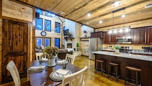 A rustic cabin interior with a wooden dining table, kitchen area, and a cozy seating area with a fireplace. - Driftaway Lodge | Luxury Broken Bow Cabin with Game Room, Hot Tub & Fire Pit (Broken Bow)