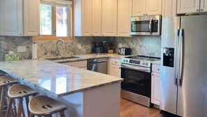 Una cocina moderna con armarios blancos, encimera de granito, electrodomésticos de acero inoxidable y taburetes de madera.