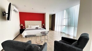 Una habitación de hotel moderna con una cama grande, un escritorio, dos sillones y un ventanal con cortinas.