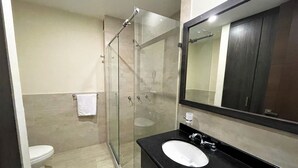 Un baño moderno con ducha envuelta en vidrio, un lavamanos negro y un espejo grande.