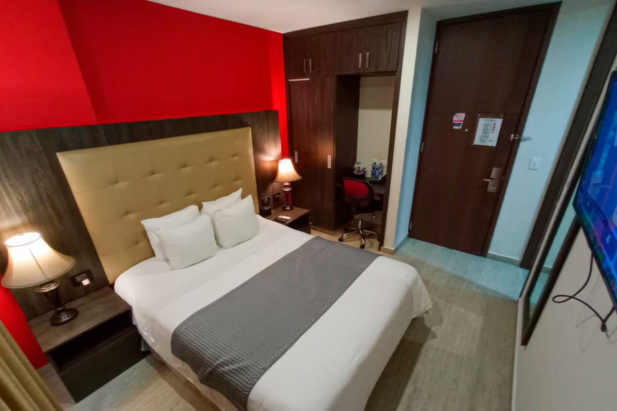 A hotel room with a large bed, a nightstand with a lamp, a wardrobe, and a television.