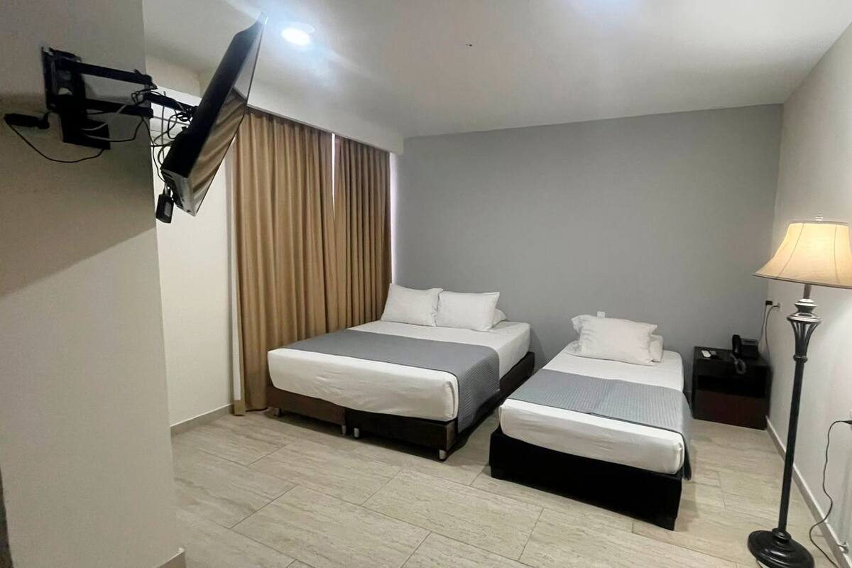 A hotel room with two beds, a TV mounted on the wall, a lamp, and a curtain.