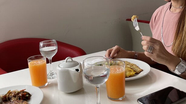 Una mesa de comedor con un plato de comida, un vaso de jugo de naranja, un vaso de agua y una tetera blanca.