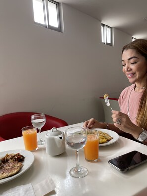 A dining table with a plate of food, a glass of orange juice, a glass of water, and a white teapot. - Hotel HR Amada Cúcuta (San José de Cúcuta)