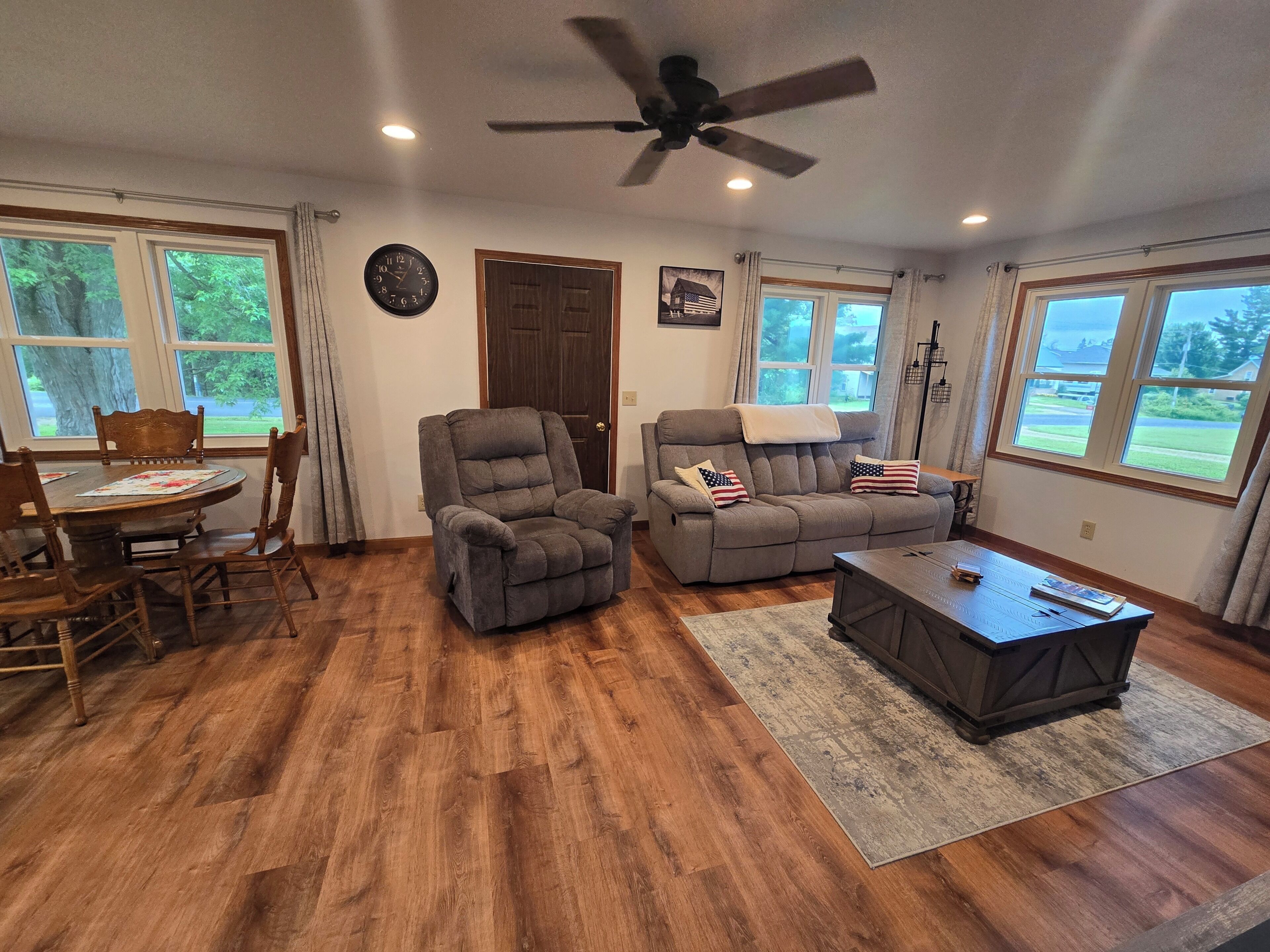 A living room with a recliner, sofa, coffee table, dining table, chairs, and a ceiling fan.
