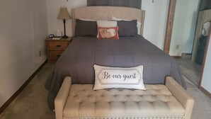 A bedroom with a bed, bedside table, lamp, and a bench with a cushion. - Hillsboro Driftless Guesthouse is cozy and ready for you! (Hillsboro)