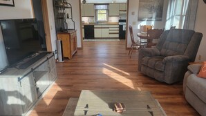 A living room with a television, a sofa, a coffee table with magazines, and a kitchen in the background. - Hillsboro Driftless Guesthouse is cozy and ready for you! (Hillsboro)