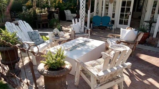 Een terras met witte Adirondack-stoelen, een rechthoekige tafel en potplanten.