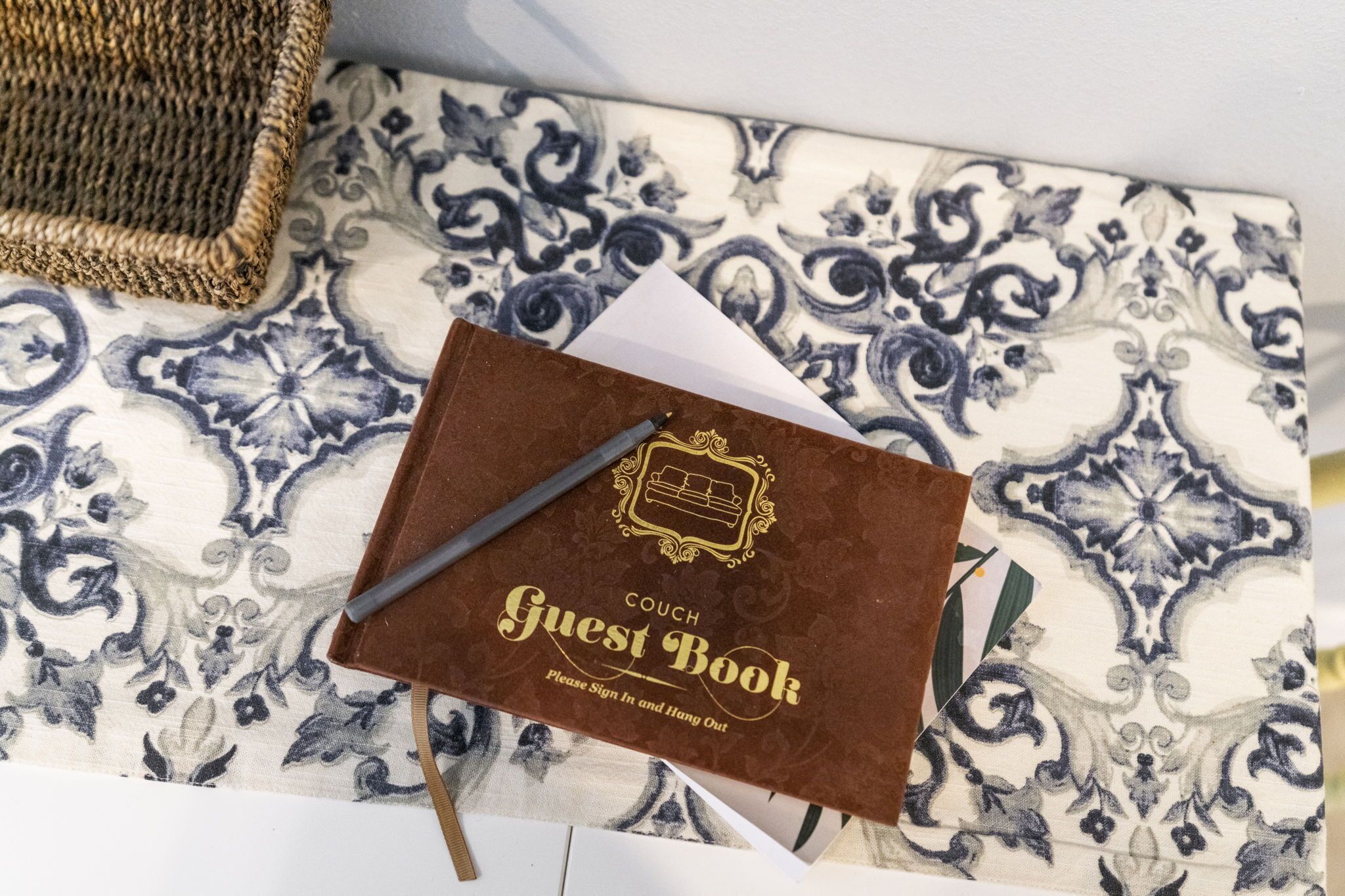 A brown guest book with a pen on a patterned tablecloth.