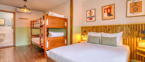 A room with a large bed, wooden bunk beds, a bathroom with a toilet, and a wooden wall with abstract art.